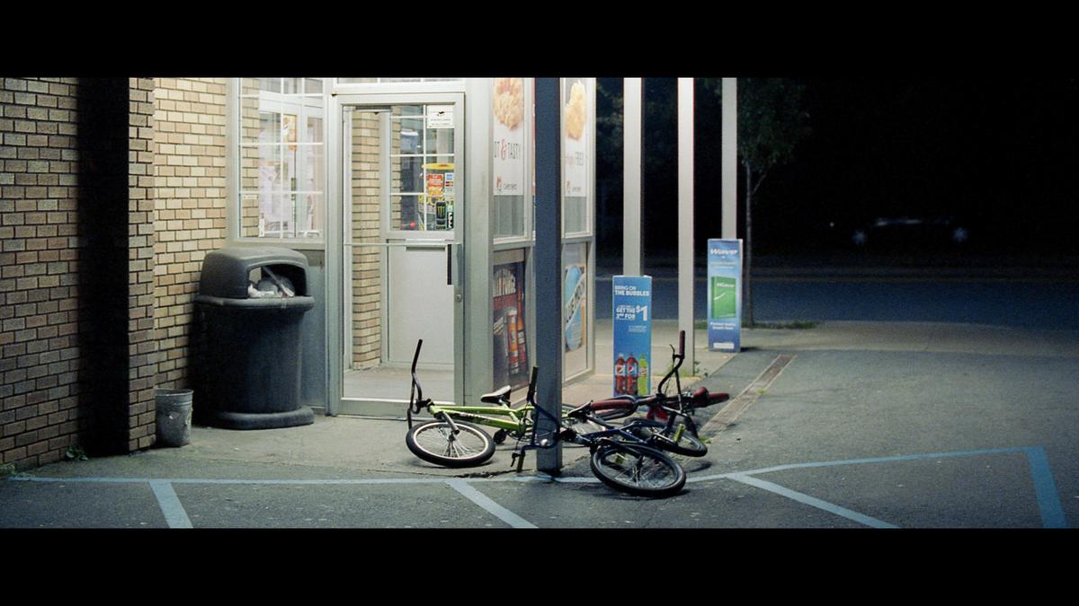 Two bicycles are lying on the ground next to a brick building with a glass door and a trash can at night.