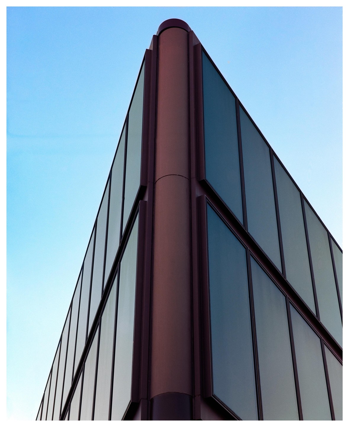 The corner of a modern building with glass windows is shown against a clear blue sky.