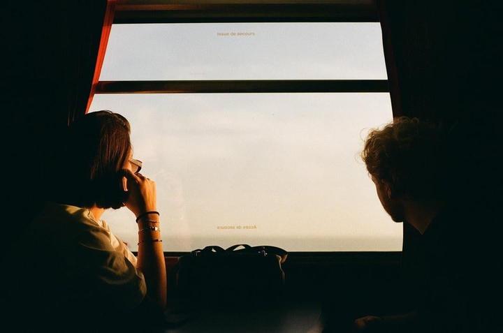 A woman and a man look out a train window at sunset.