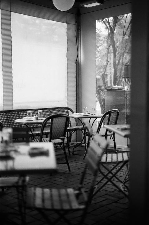 A cafe interior with tables and chairs is visible through a window, with trees and a building in the background.