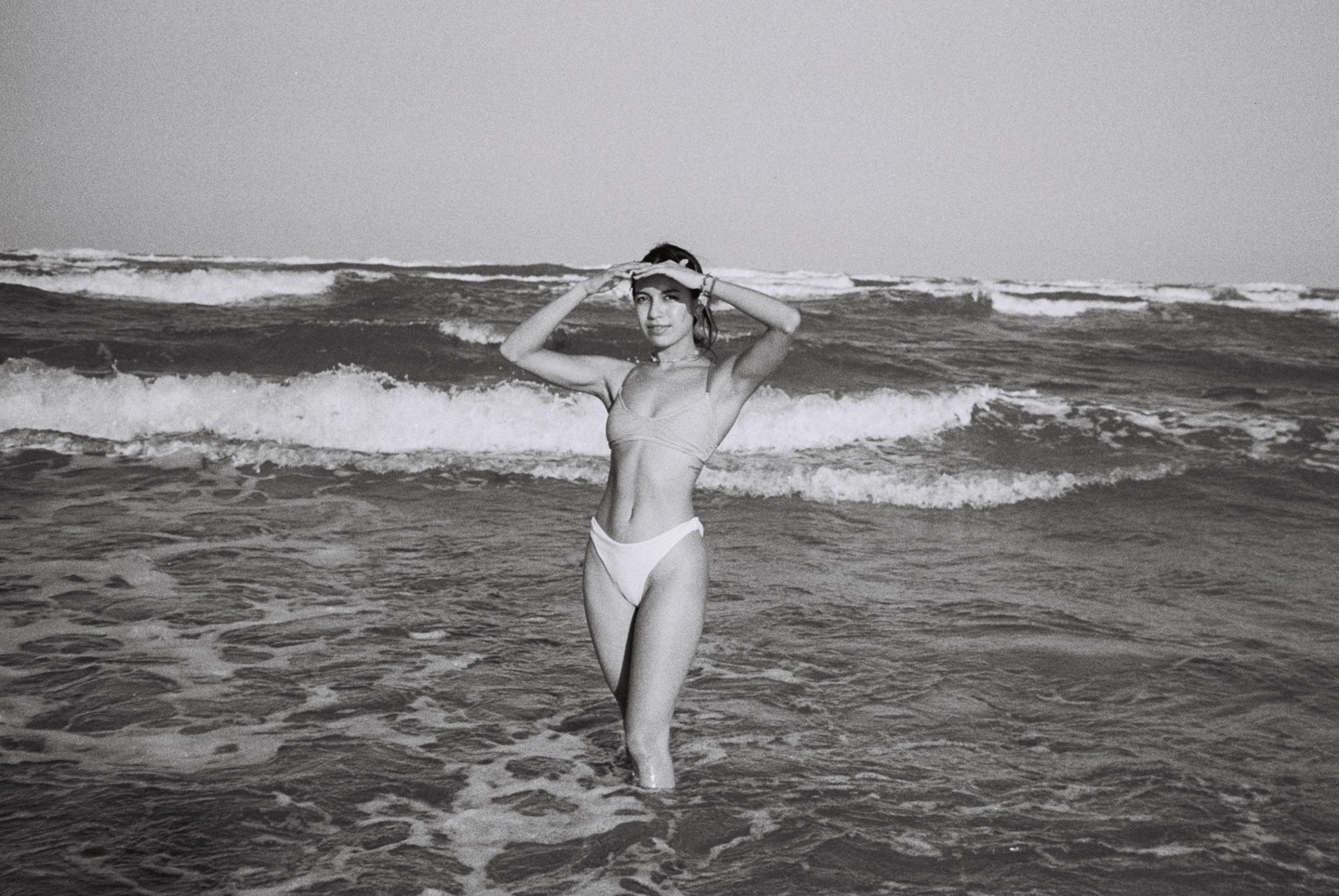 A woman stands in the ocean with waves crashing around her.