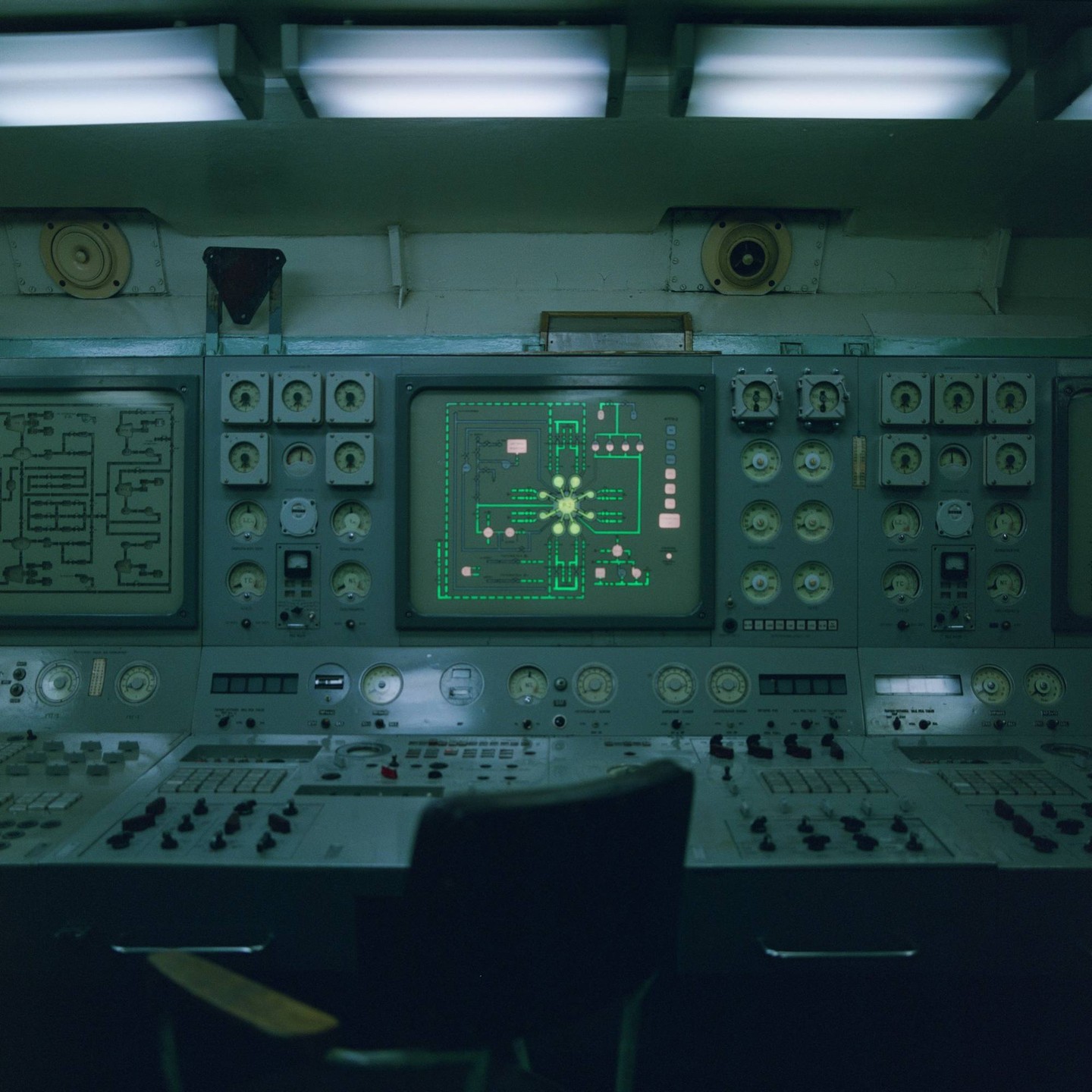 A control panel with multiple gauges and screens, one displaying a green diagram, is shown with a chair in the foreground.