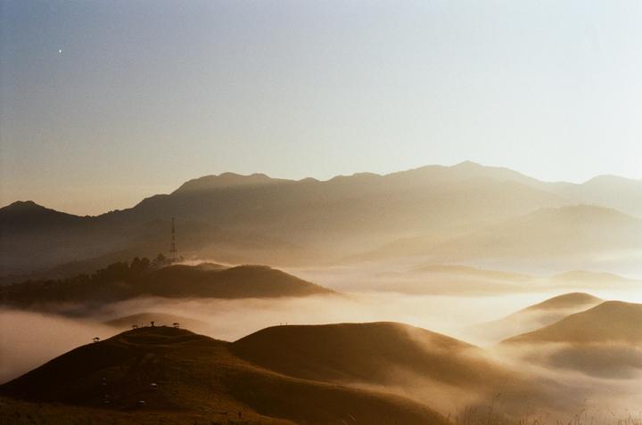 A crescent moon hangs in the sky above a mountainous landscape covered in fog during sunrise.