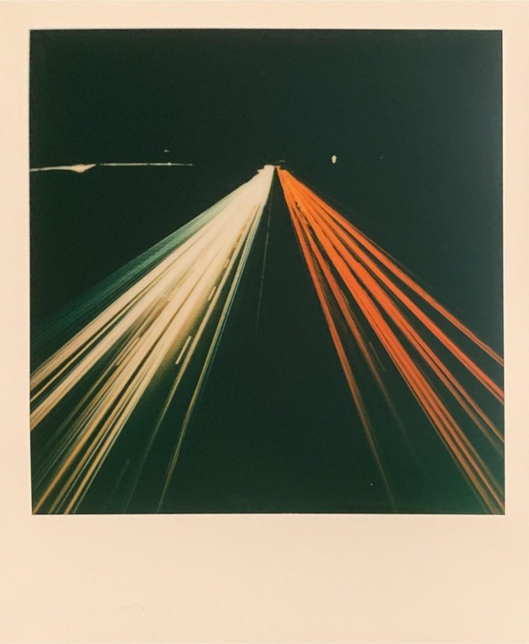 Light trails from vehicles on a highway at night create streaks of white, green, and orange against a dark background.