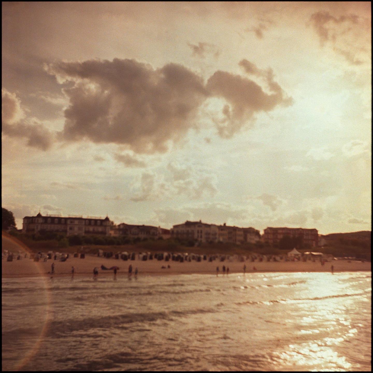 A beach with people and buildings in the distance is visible under a cloudy sky.