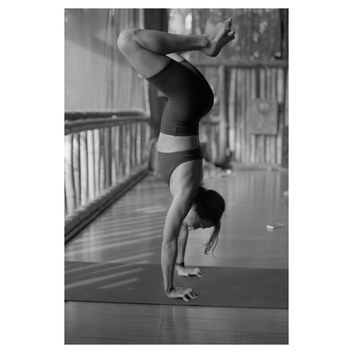 A woman in athletic wear performs a handstand on a yoga mat indoors.
