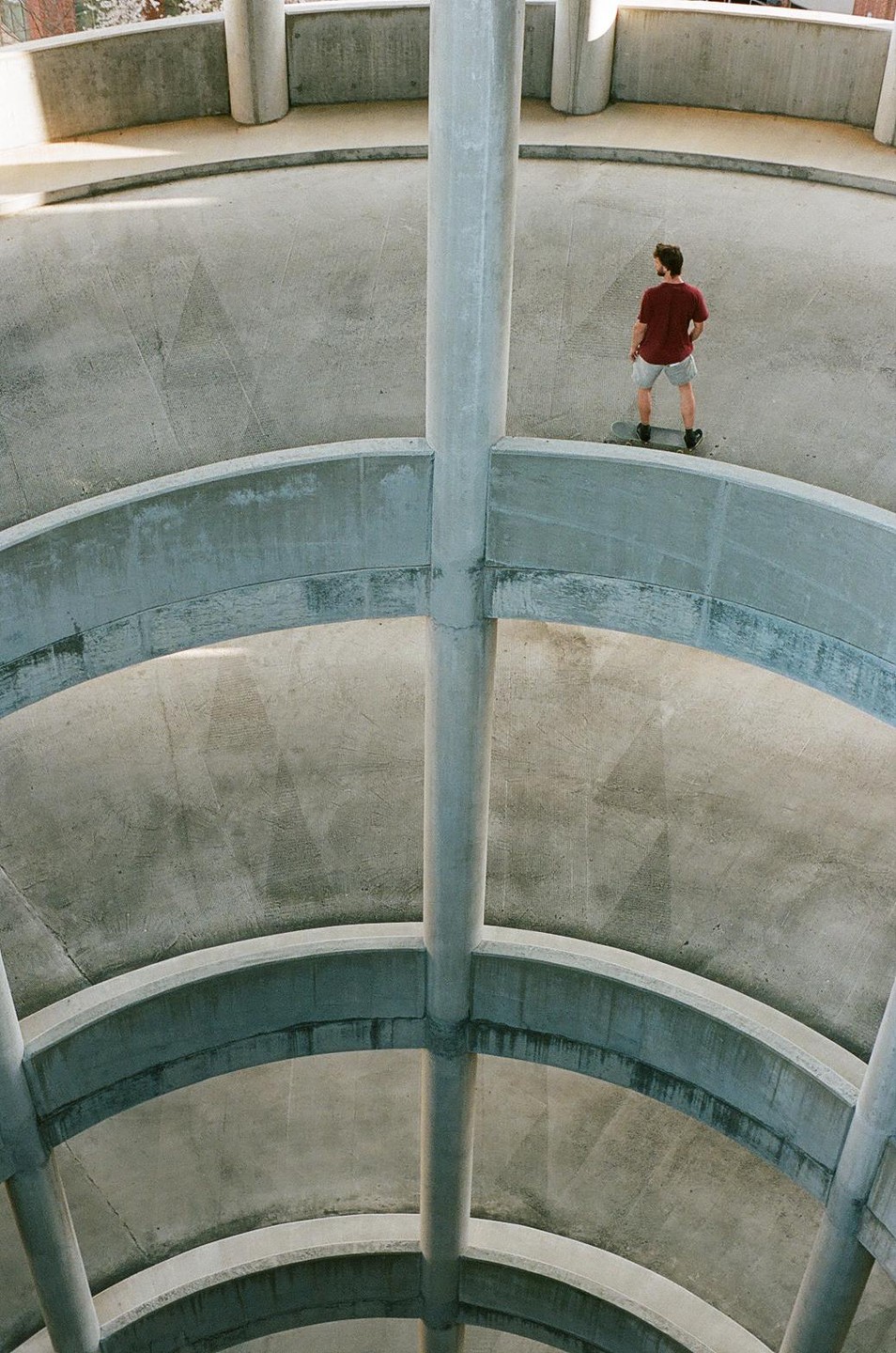 A man stands on a skateboard in a concrete parking garage.