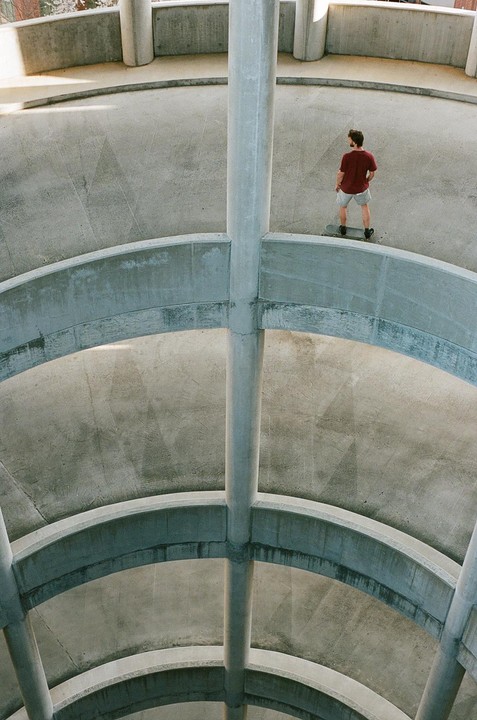 A man stands on a skateboard in a concrete parking garage.