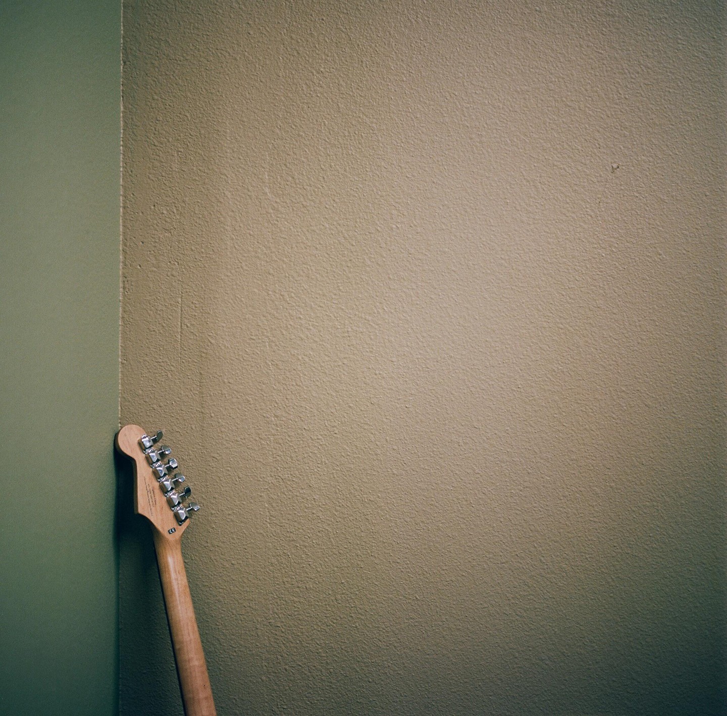 The headstock of a guitar leans against a corner where two walls meet.