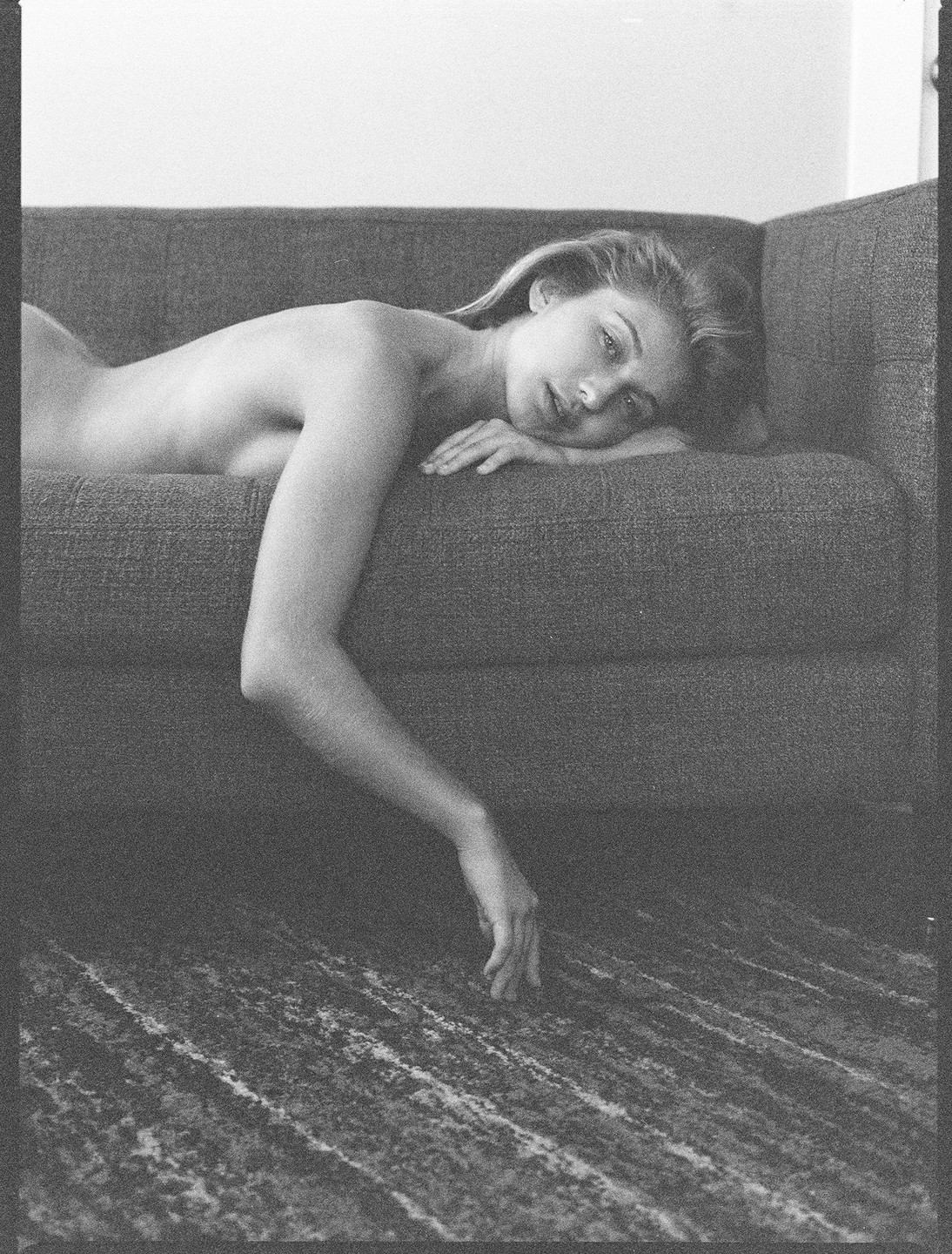 A woman lies nude on a sofa with her arm draped towards the floor in a black and white portrait.