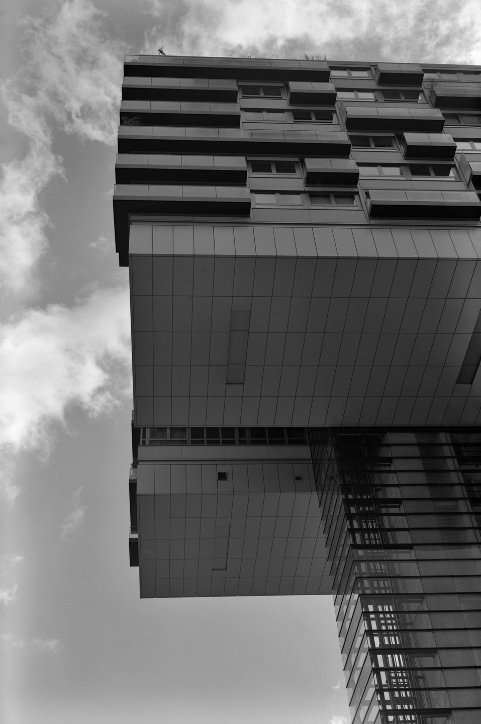 A modern building with a cantilevered section and many windows is shown against a cloudy sky.