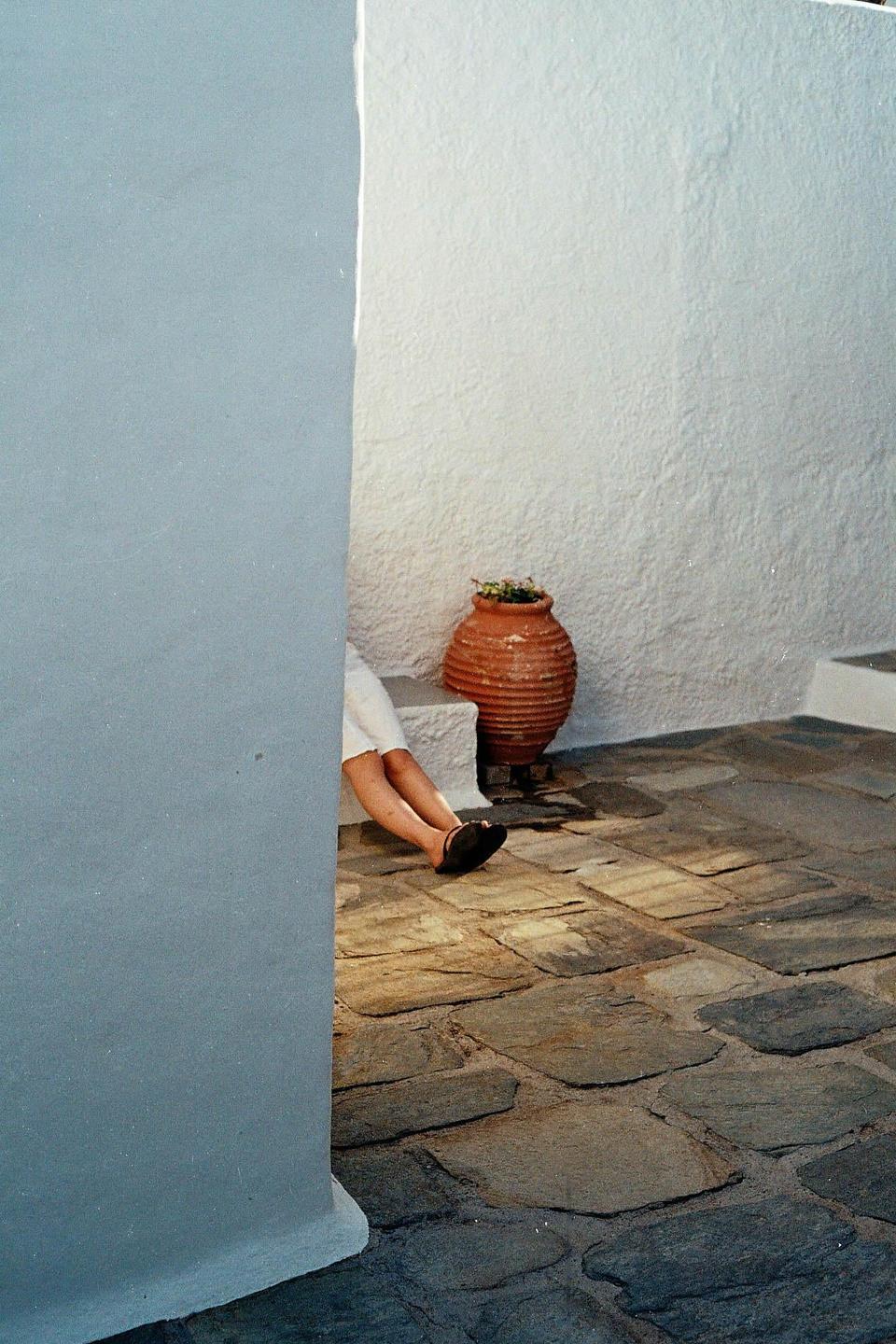 A person's legs are visible next to a terracotta pot on a stone patio, partially obscured by a light blue wall.