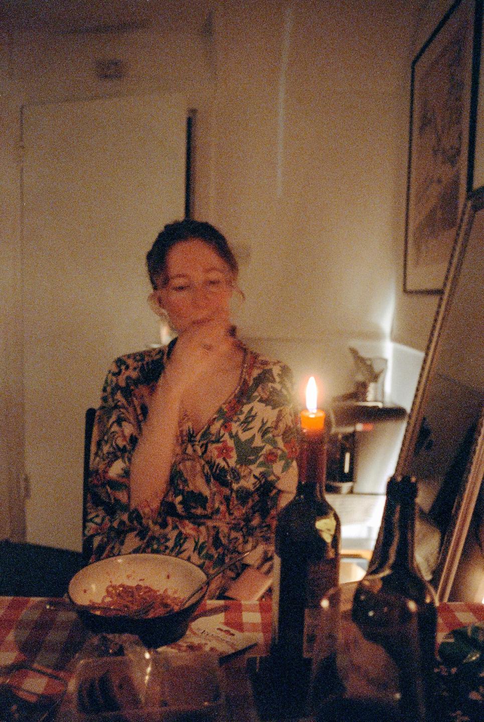 A woman sits at a table with a lit candle and a bowl of food.