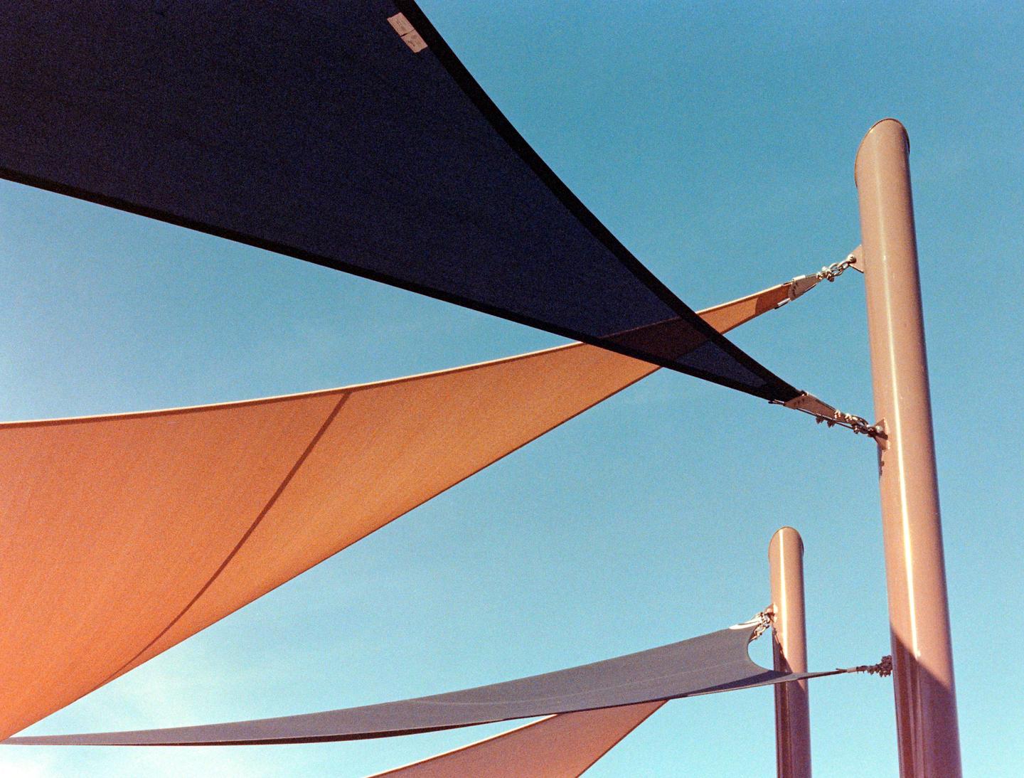 Shade sails are attached to poles against a clear blue sky.