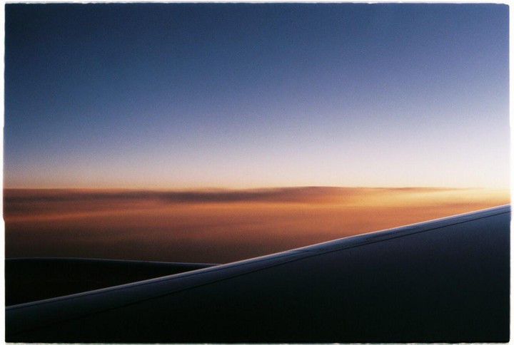 An airplane wing is visible against a sky with a gradient of blue to orange.