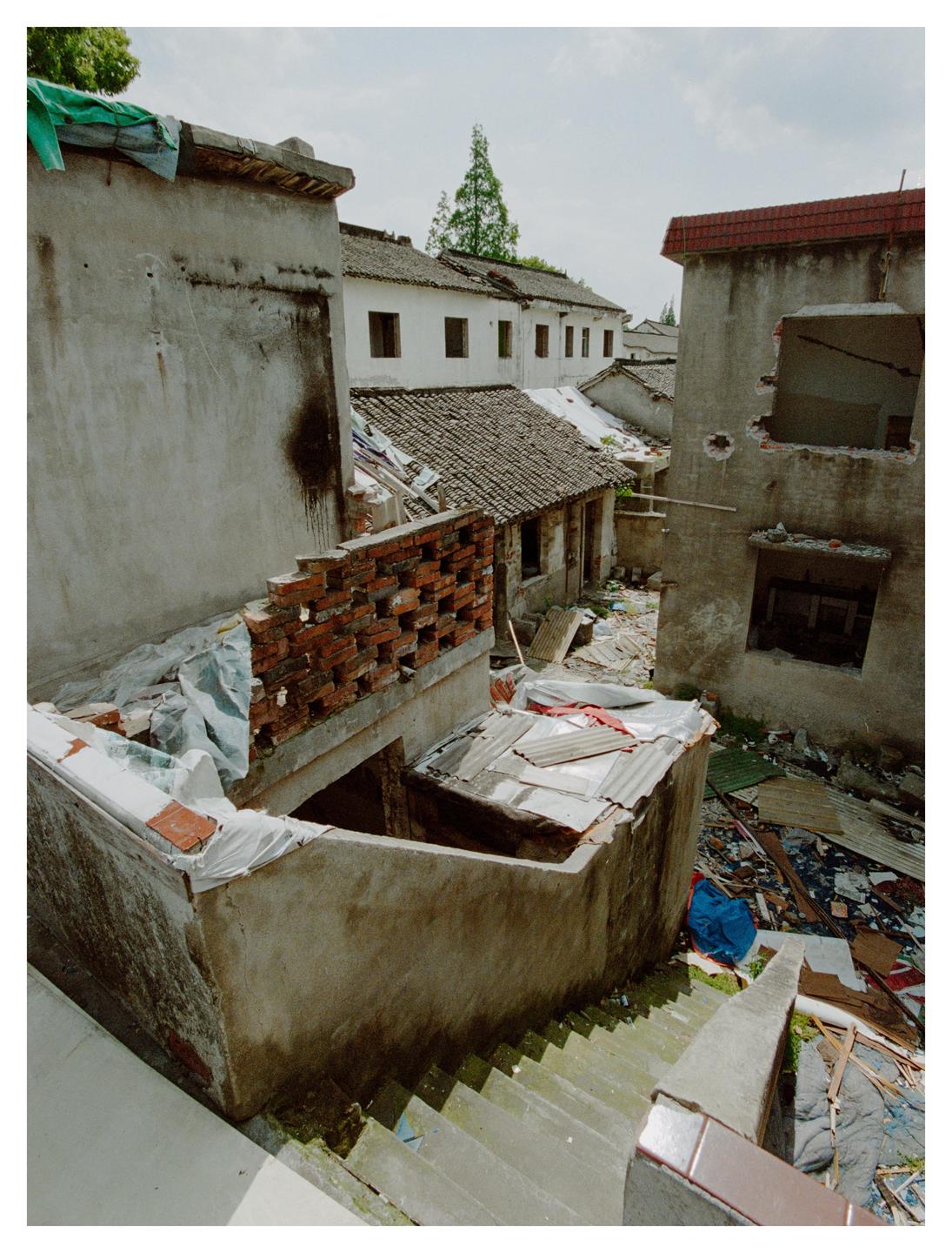 A narrow alleyway is surrounded by dilapidated buildings and debris.