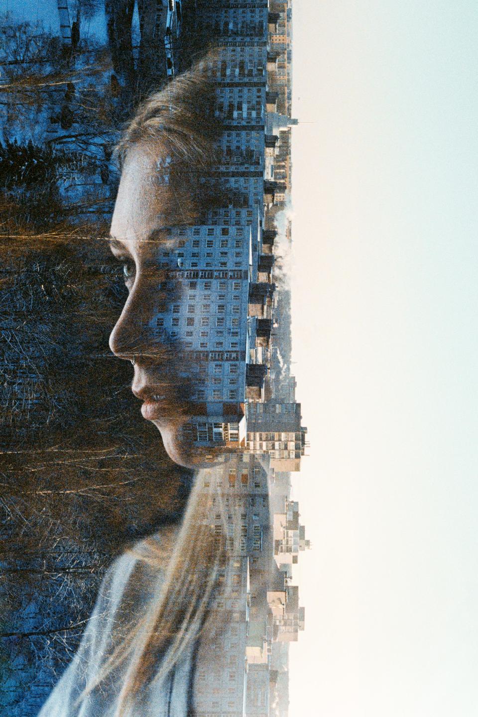 A woman's profile is double exposed with a cityscape and a forest.