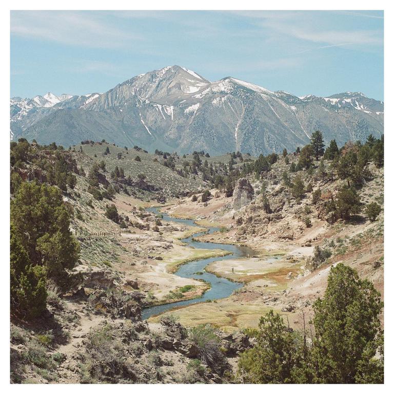 A winding river flows through a valley with snow-capped mountains in the background.