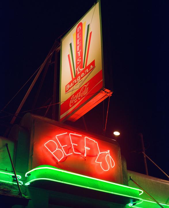 A neon sign for Beefy's Burgers glows red and green against a dark night sky.