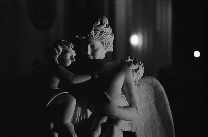 Three statues of people are illuminated by a light source in a dark room.