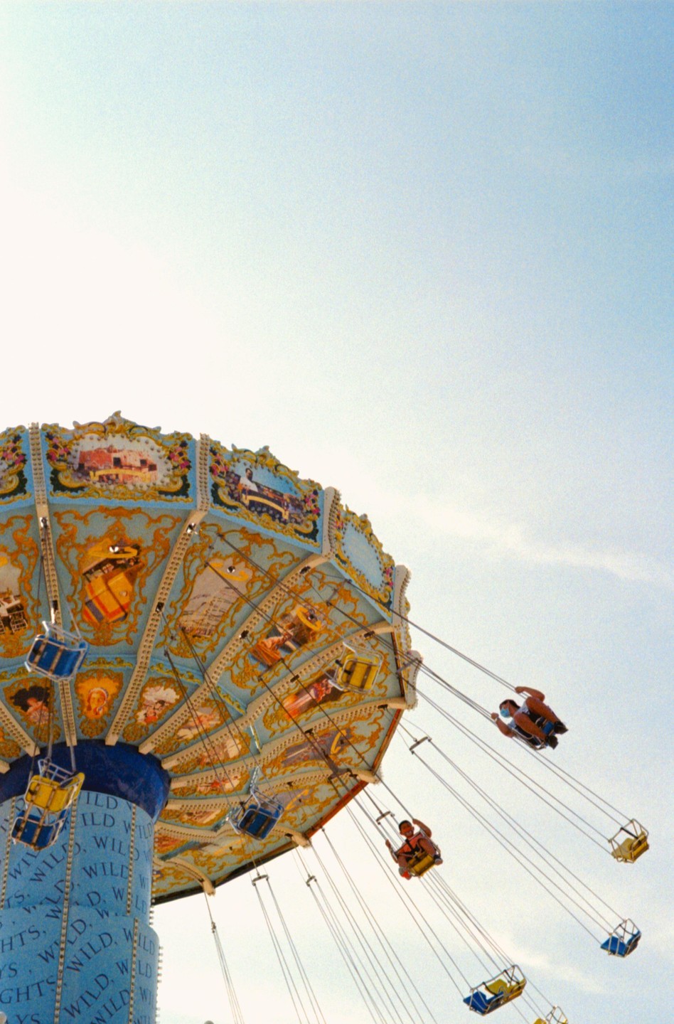 A swing ride with people on it is captured from a low angle against a clear sky.