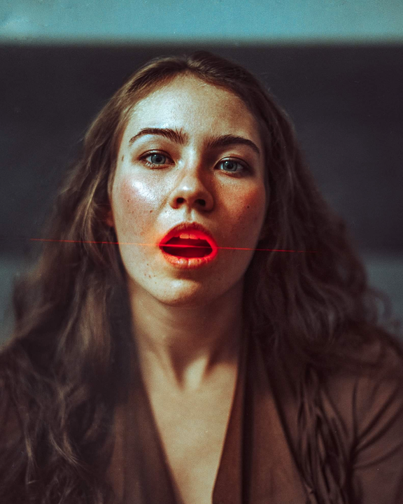 A woman with long hair and freckles has a red laser beam shining across her face and into her open mouth.