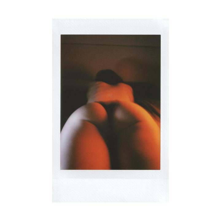 A woman is lying on her stomach, seen from behind, with warm light illuminating her body.