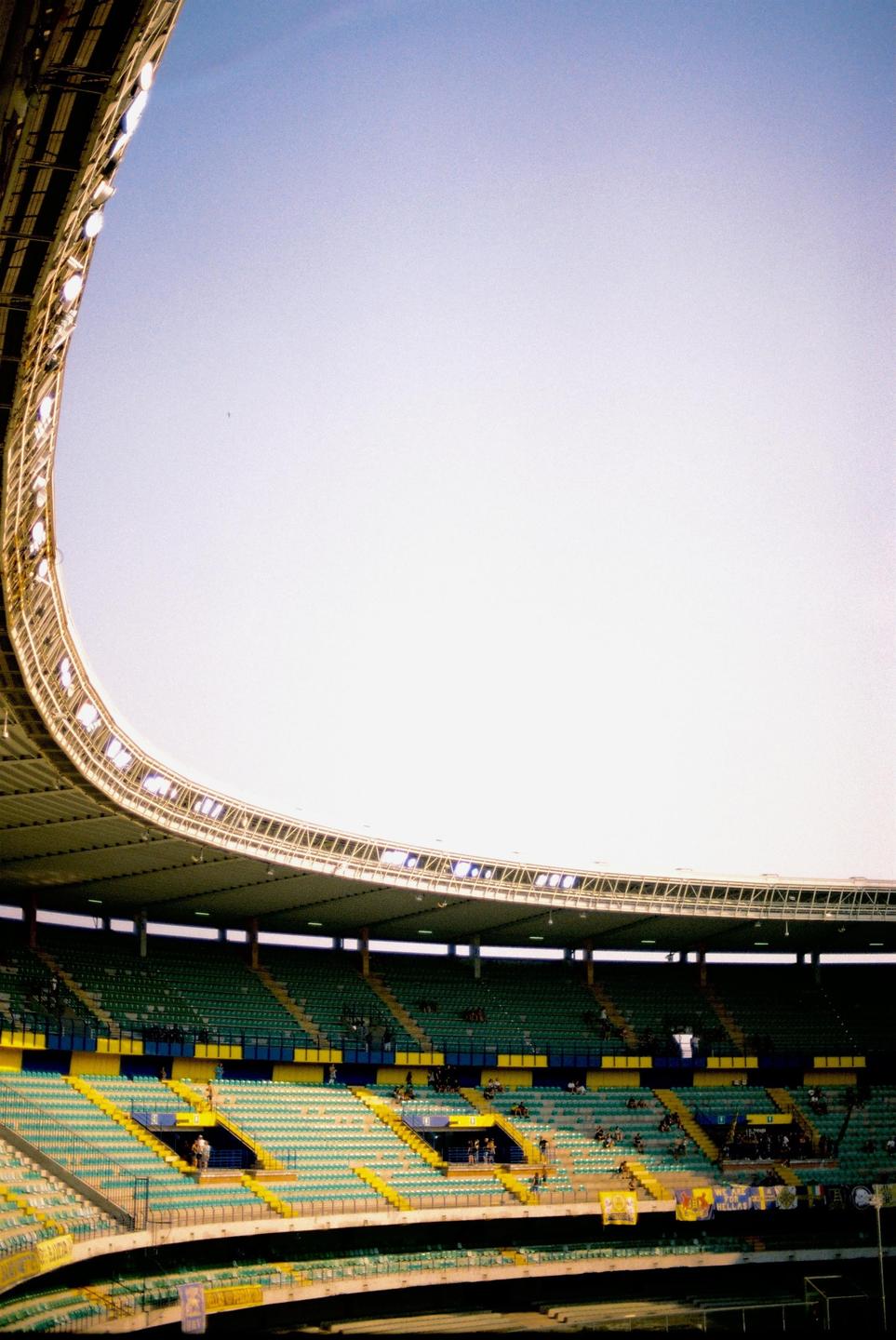 A large, empty stadium with green and yellow seats is visible under a bright sky.