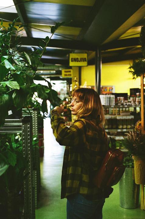 A woman wearing glasses and a plaid shirt is looking at plants in a store.