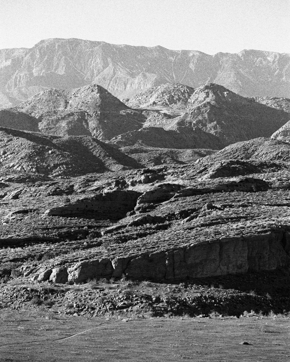 A black and white landscape shows a vast mountain range under a bright sky.