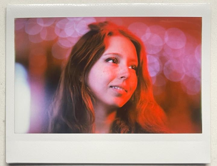 A woman with long hair looks to the side, illuminated by red light with bokeh in the background.