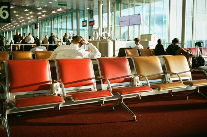 People are waiting in an airport terminal with rows of red and tan seats.