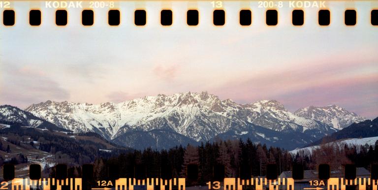 A panoramic view shows snow-capped mountains and a forest under a colorful sky.