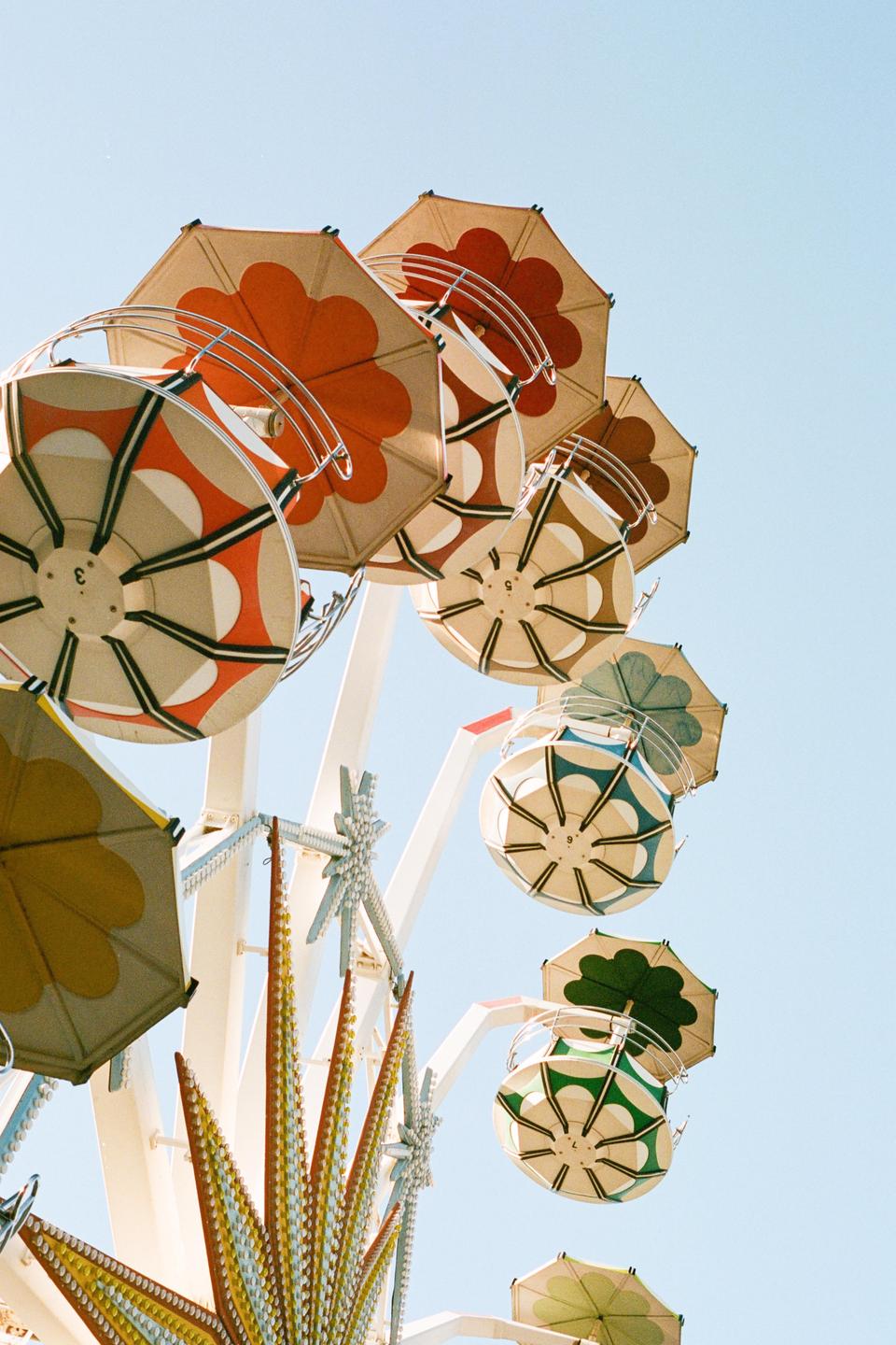 A ferris wheel with colorful umbrella-like seats is set against a clear blue sky.