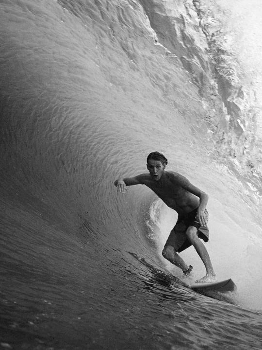 A man surfs a large wave, riding inside the barrel of the wave.