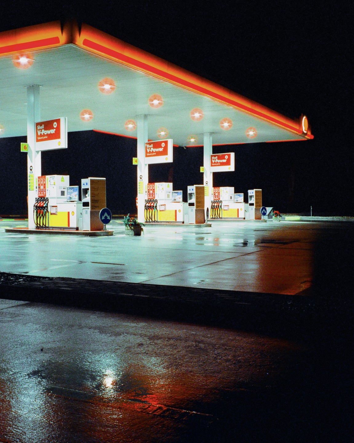 A gas station with multiple pumps is illuminated at night, with reflections on the wet ground.