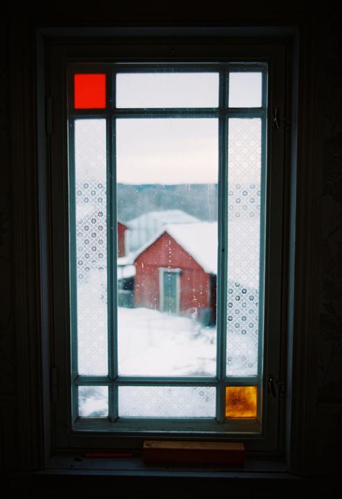 A red barn is visible through a window with stained glass accents on a snowy day.