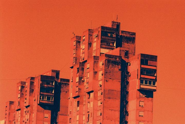 A tall, brutalist apartment building stands against an orange sky.