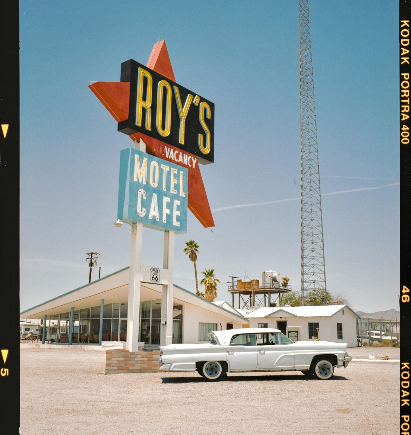 A white vintage car is parked in front of Roy's Motel and Cafe sign and building.