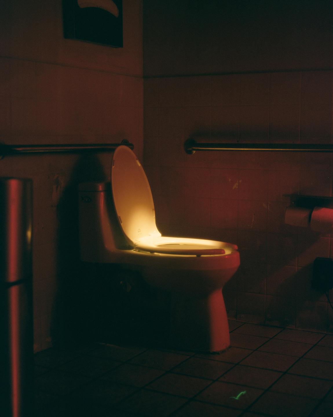 A toilet with its lid open is illuminated by a warm glow in a dimly lit bathroom.