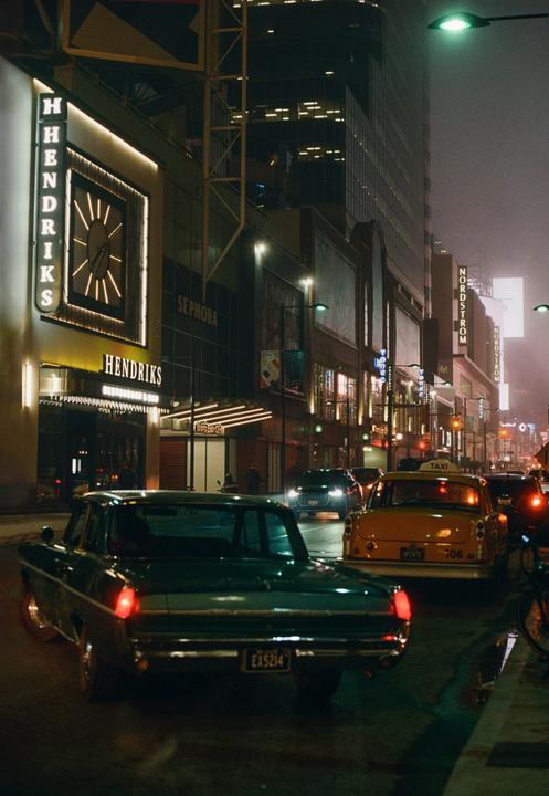 A street at night is filled with cars and illuminated by neon signs and streetlights.