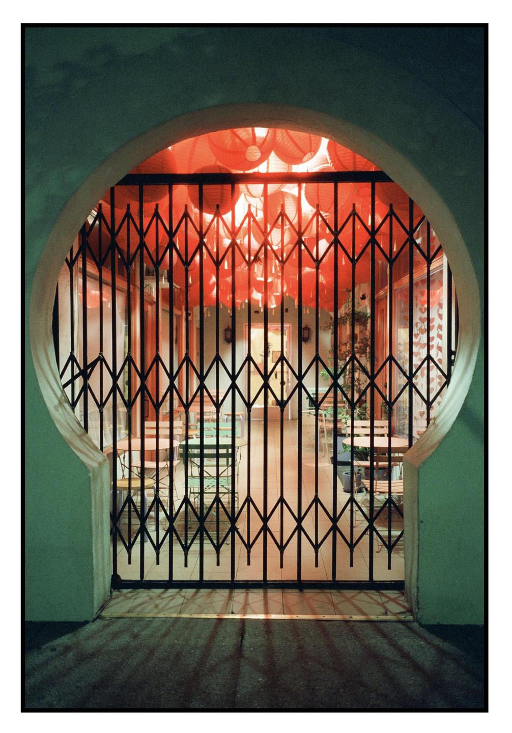 A closed gate with a pattern of red lanterns visible through it.