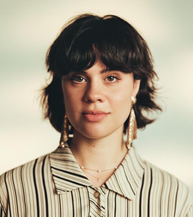 A woman with short dark hair and large earrings looks directly at the viewer.