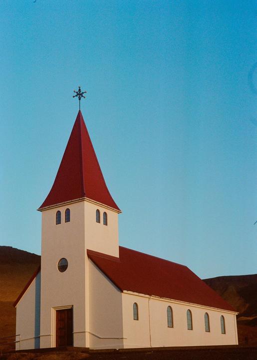 A white church with a red roof and steeple stands against a clear blue sky.