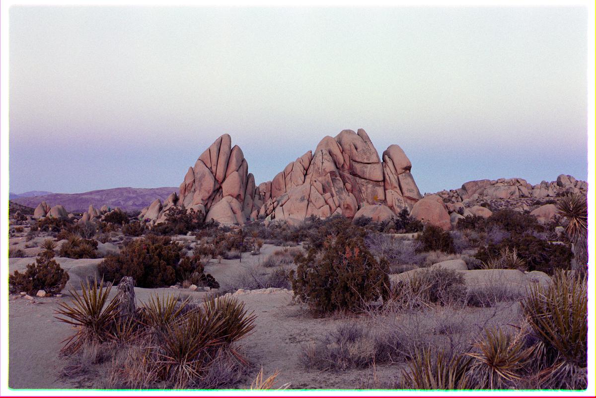 A desert landscape features large rock formations and sparse vegetation under a pale sky.