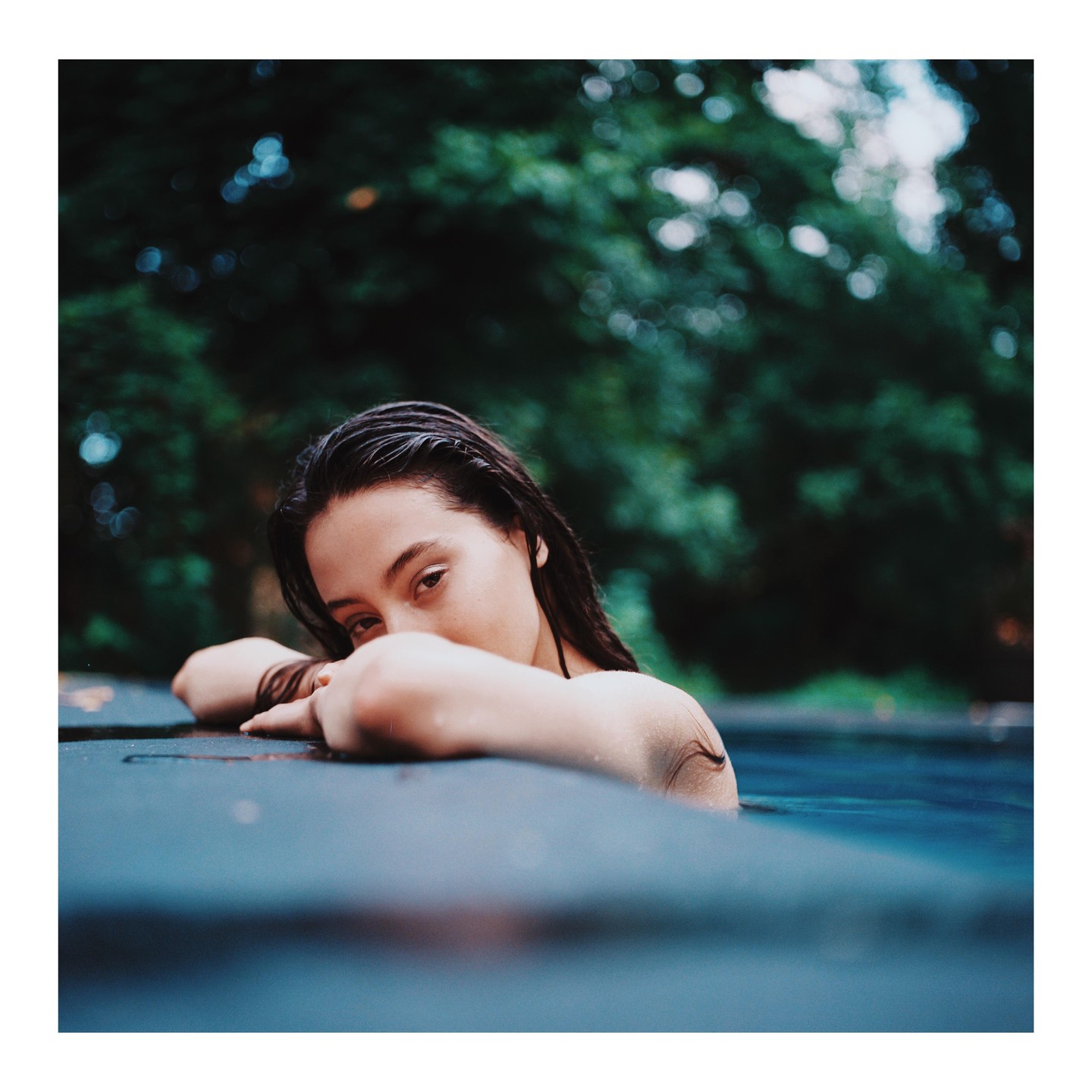 A woman with wet hair rests her arms on the edge of a swimming pool.