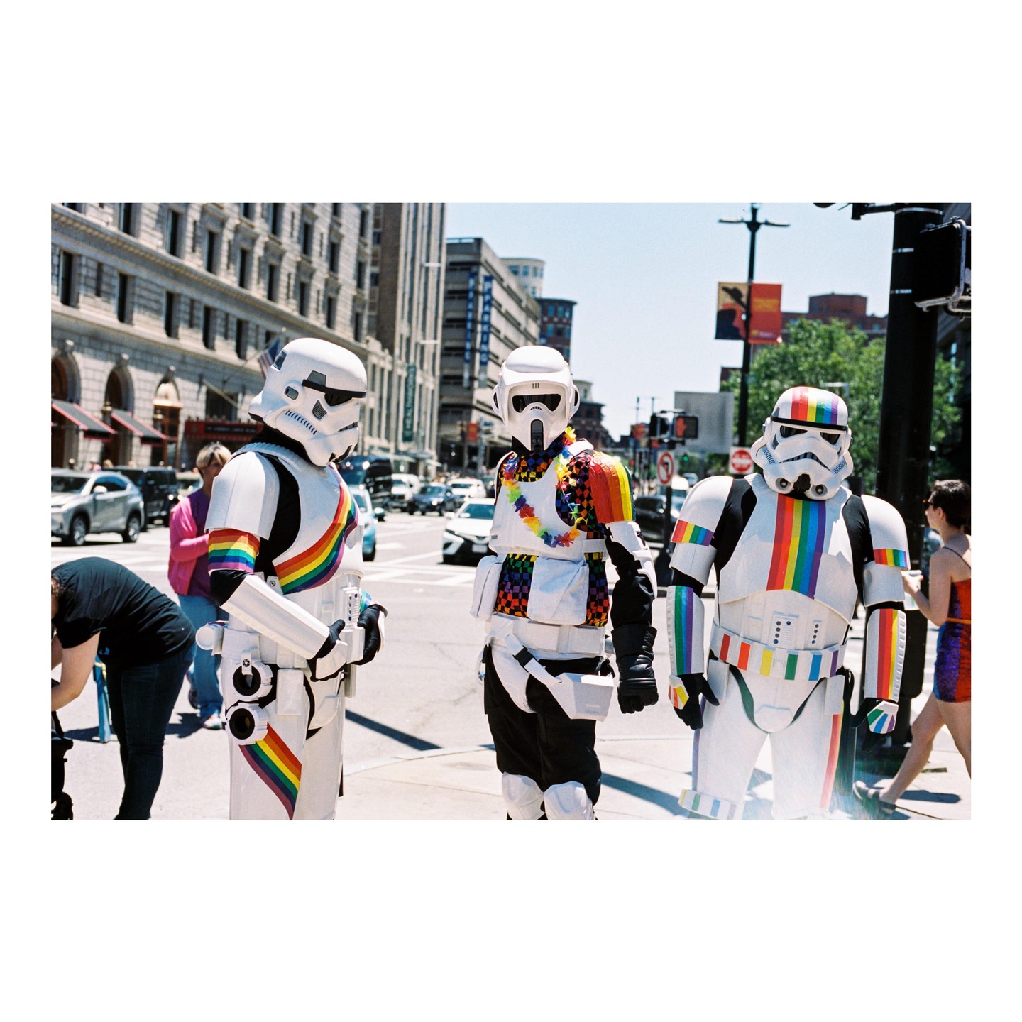 Three people in stormtrooper costumes with rainbow accents stand on a city street.
