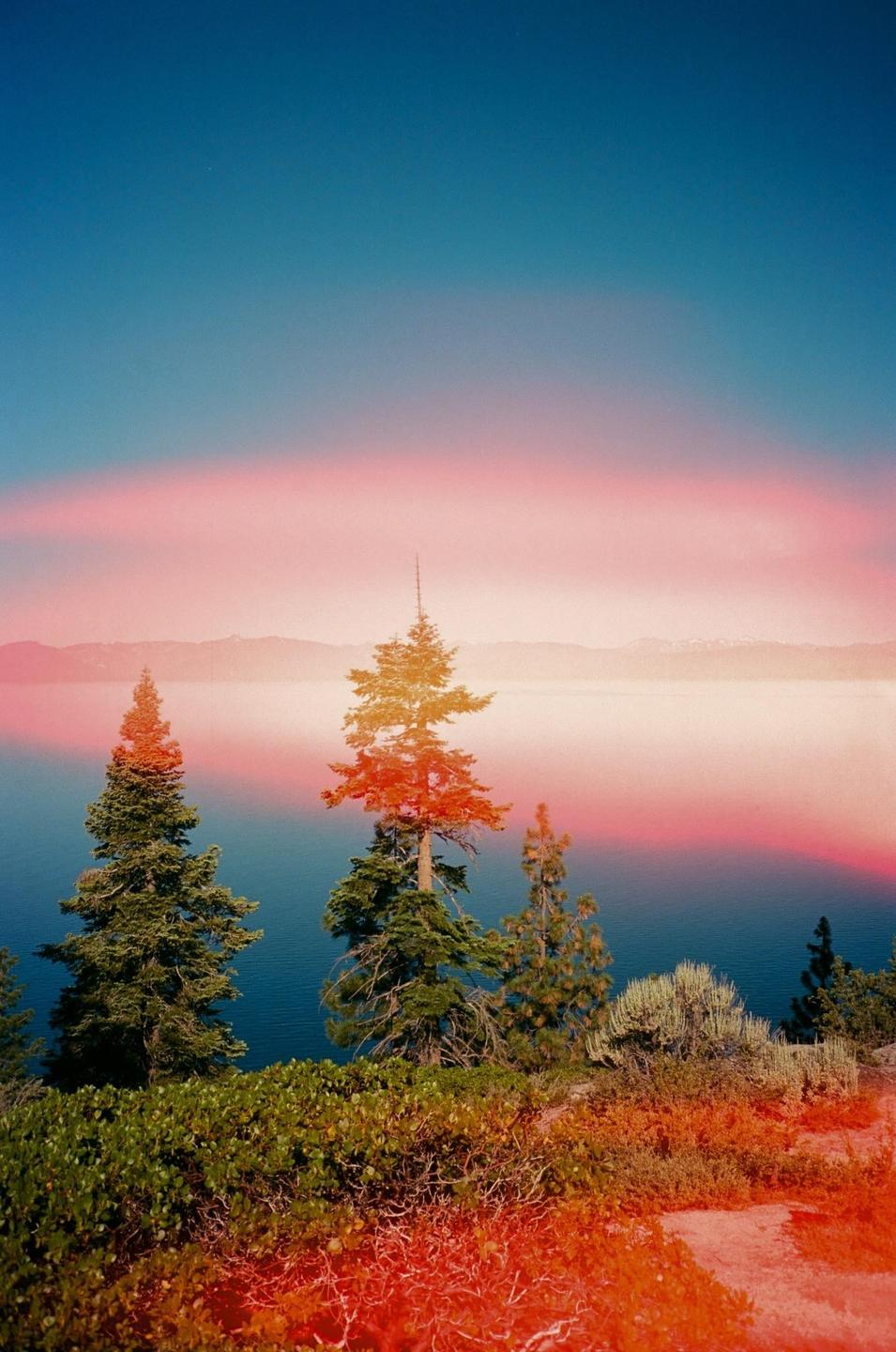 A vibrant landscape shows a lake surrounded by trees and mountains under a colorful sky.
