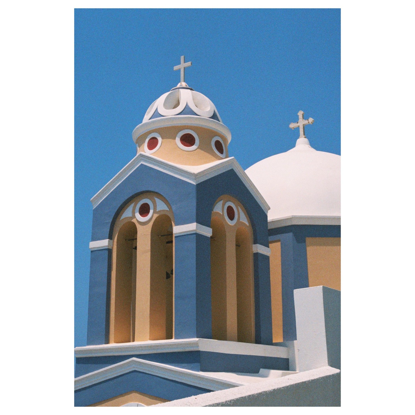 Two blue-domed churches with white crosses on top stand against a clear blue sky.