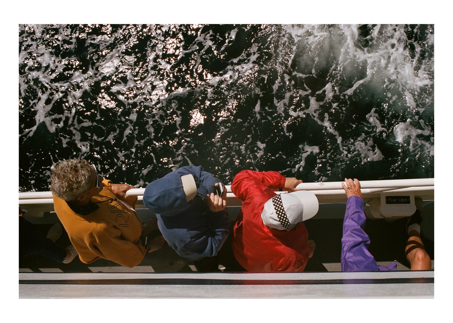 Three people are looking down at the foamy water from a boat.